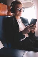 Wall Mural - caucasian woman dressed in formal wear use mobile phone inside airplane sitting on passenger seat, s