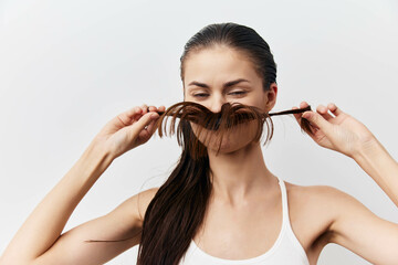 Wall Mural - Creative hairstyle concept with a woman playfully holding her hair to form a mustache shape, showcasing a playful and fun attitude on a light gray background