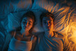 © TRAVELARIUM - Couple lies in bed under dim lighting, woman is peacefully asleep while man is awake and has insomnia because of lot of thoughts, emphasizing mental burden of unresolved worries, top view