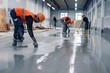 © Pete - Construction workers on site, painting grey epoxy resin on concrete floor. Man in orange vest, hard hat, painting with brush. Other workers in blue, black hard hats, working in industrial hall.