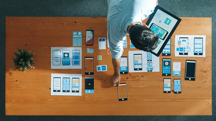 Top down view of software developer holding tablet while choosing icon for mobile phone interface or software program. Start up manager using Ux Ui design to develop wireframe prototype. Convocation.