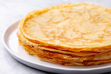 Wall Mural - Crepes, thin pancakes with honey on a white plate. Marble background. Close up.