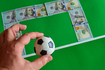 A souvenir soccer ball against the background of hundred-dollar bills shaped like soccer goals on a green background, online sports betting, money for soccer matches, bookmaker bets