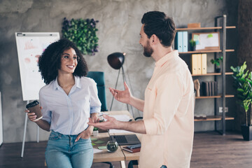 Wall Mural - Photo of two young colleagues drink coffee chatting loft interior office business center indoors