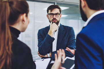 Male trader in formal wear puzzled on ideas for productive strategy of development business company with professional colleagues, executive managers cooperating on startup project in office