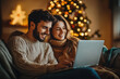 © Artem Zatsepilin - couple shopping online using laptop, sitting on sofa in living room, dim evening light, cozy blankets and Christmas tree in background. new year sale poster