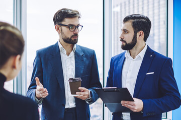 Male and female company workers in formal wear communicating and discussing business news in financial world, accomplished professional colleagues collaborating togetherness in light office