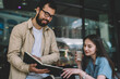© BullRun - Positive smiling male and female students enjoying time in coffee shop while checking schedule for private lessons in textbook for education, successful friends reading information from notepad