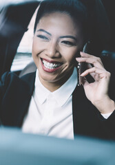 Happy cheerful manager driving luxury car and having business call via smartphone application connected to roaming internet, excited woman enjoying international conversation with colleague