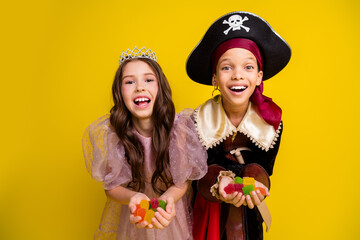 Poster - Photo of two kids halloween princess pirate costume arms hold marmelade isolated on yellow color background