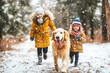 © pilipphoto - Happy active family with kids walking their pet dog golden retriever in the snowy winter forest