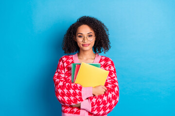 Poster - Photo of american beautiful girl with curly hair wearing eyeglasses intelligent student holding copybooks isolated on blue color background