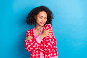 Poster - Portrait photo of american beautiful girl with curly hair wearing red stylish cardigan hugging herself isolated on blue color background