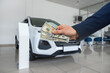 © RomanR - business man gives dollar cash when buying a car at showroom. Concept of purchase or rent vechicle