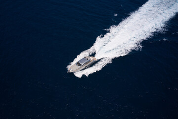 Gray yacht moves fast on dark sea water making white trail, aerial view. Yacht in motion on dark water, aerial view.