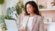 © World of AI - young East Asian woman in a plaid blazer and wide-leg trousers, typing on her laptop at a standing desk in a trendy startup office