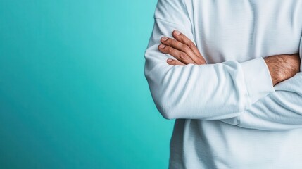 an individual wearing a white sweater stands with arms crossed against a teal background, epitomizin