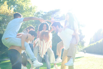 Cheerful young people enjoying a sunny day at the park, giving piggyback rides to each other