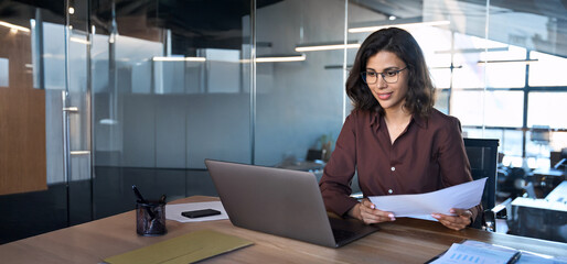 focused latin hispanic business woman working on laptop computer reading financial document report i