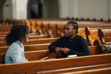 Priest holding rosary beads listening to young man in church