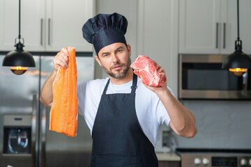 Portrait of attractive man preparing fresh natural meal at kitchen home indoors. Handsome cheerful man preparing raw fish and meat, salmon and beef. Healthy food, cooking concept.