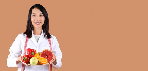 Poster - Female Asian nutritionist with vegetables and fruits on brown background with space for text