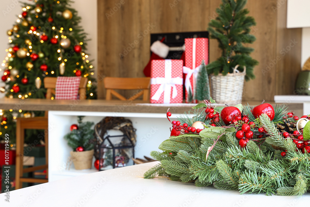 Christmas wreath with red apples and berries on white table in kitchen