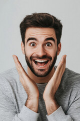 A man with a big smile on his face is making a gesture of excitement. He is wearing a gray shirt and has a beard