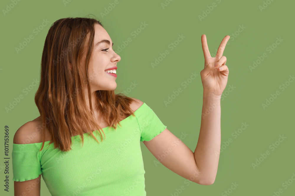 Pretty young woman showing peace gesture on green background