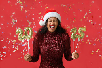 Wall Mural - Happy African-American woman in Santa hat and with figure 2025 made of balloons on red background. New Year celebration