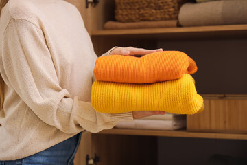 Canvas Print - Young woman putting stack of stylish clothes on shelf in closet, closeup