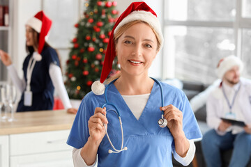 Wall Mural - Mature female doctor in Santa hat with stethoscope at hospital on Christmas eve