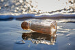 © Matthew Roharik - Handwritten letter message in glass on bottle washed up on sand beach with waves and ocean water in the background.