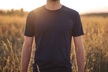 Canvas Print - A person stands in a field during sunset, wearing a dark t-shirt, surrounded by tall grass.