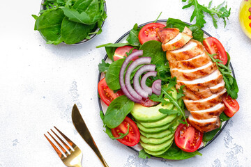 Grilled chicken fillet with avocado, spinach and tomato garnish, white background, top view