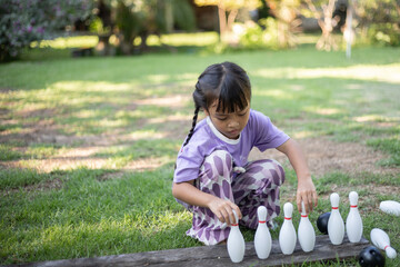 A young girl is sitting on the grass and playing with a set of bowling pins