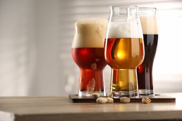 Poster - Glasses with different types of beer and pistachio nuts on wooden table indoors, closeup. Space for text