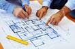© saichon - A photo of two people, one holding blueprints and the other pointing at them with their finger on top, with building plans spread out in front showing an apartment floor plan.