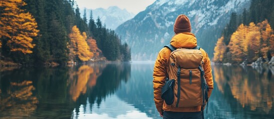 Wall Mural - a lone hiker stands by a tranquil lake surrounded by mountains and vibrant autumn foliage, gazing at