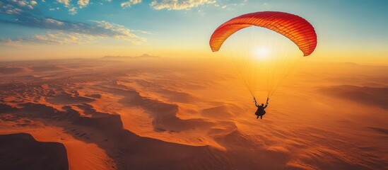 Poster - A paraglider soars over a desert landscape at sunset. The sun shines brightly in the sky, and the dunes stretch out in the distance.