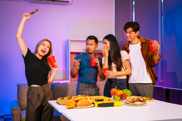 Four Asian friends, two men and two women, celebrate in an office party. They enjoy a fun-filled night with food, drinks, and laughter, bonding over teamwork and friendship.