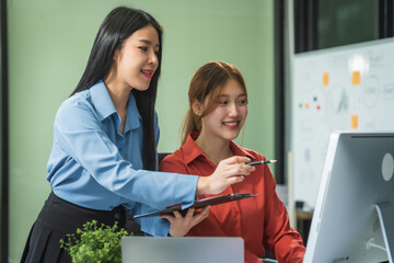 Two Asian business woman work at a desk, discussing business strategies, marketing, plans.They analyze money matters explore how to write a clear, easy-to-understand business plan for future growth