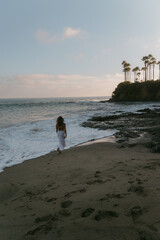 Wall Mural - Woman walking on sand next to waves during sunset