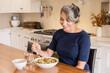© Cavan Images - Woman smiling at her fruit salad in the kitchen