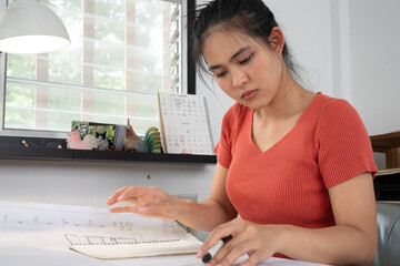 Young beautiful woman sitting at desk working with computer in home office. Asian female architect freelance work from home using internet technology to check new project document online. copy space.