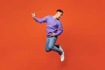 Sticker - Full body side view young happy man of African American ethnicity he wear purple sweatshirt casual clothes jump high play air guitar isolated on plain red orange background studio. Lifestyle concept.