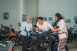 © Odua Images - Asian man holding the handlebar of a new motorcycle with his wife and saleswoman looking at the price list in the showroom