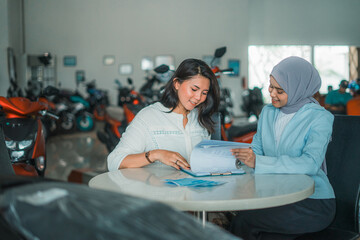 customer sits with a veiled female shop assistant chatting in a motorcycle showroom