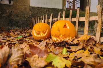 ground level view of two Halloween pumpkins on fallen tree leaves, street decoration