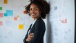 © Oulaphone - A confident woman smiles by a wall covered in notes and charts, showcasing a professional and creative environment.